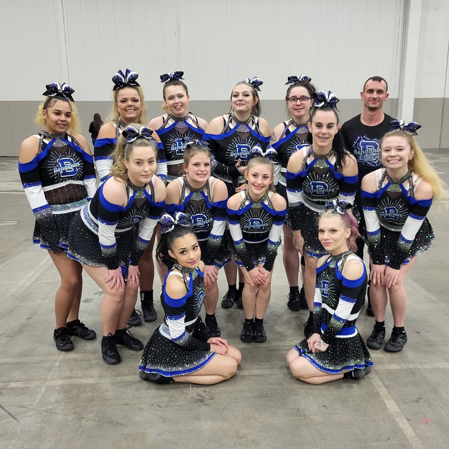 Cheer team and coach posing together in matching royal blue, black, white, and silver uniforms