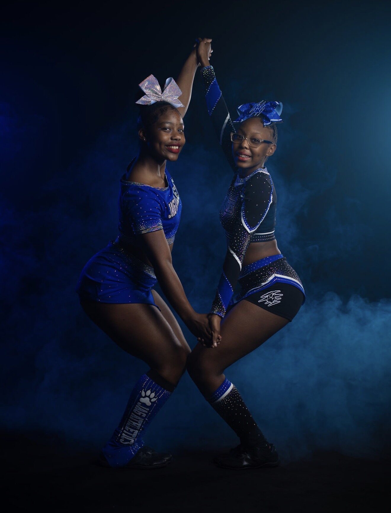 Two cheer athletes modeling coordinating royal blue and black JAG Athletics uniforms