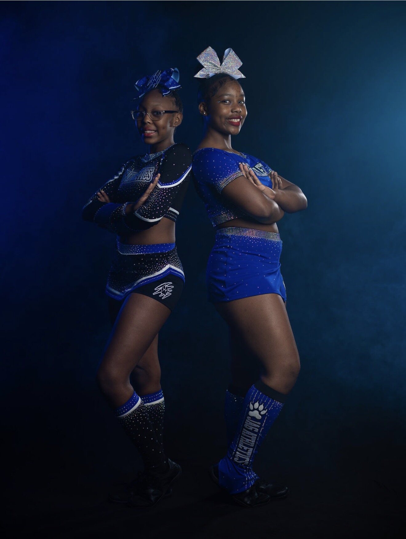 Two cheer athletes standing back to back in coordinating JAG Athletics uniforms