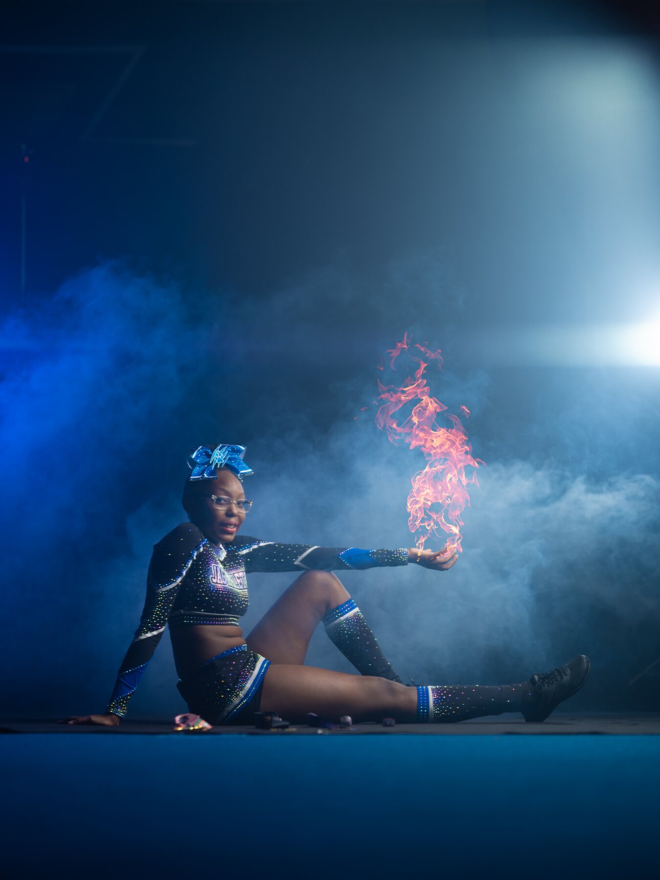 Cheer athlete in a rhinestone black and blue uniform posing with a flame effect