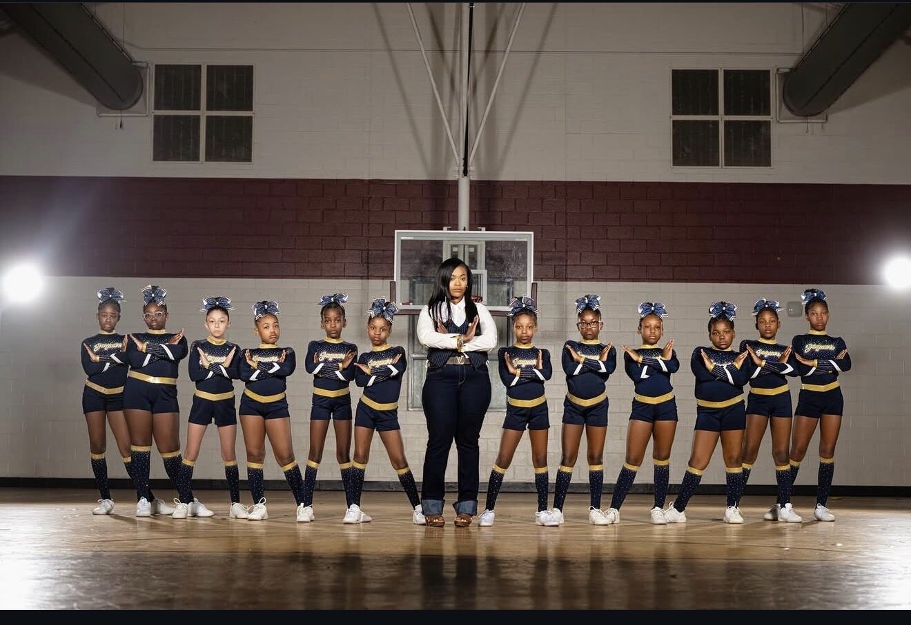 Cheer program lined up in coordinating navy and gold uniforms with their coach