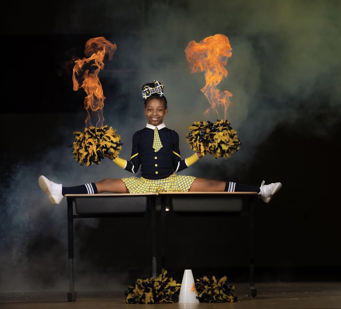 Cheer athlete performing a split in a navy and yellow themed uniform with pom-poms