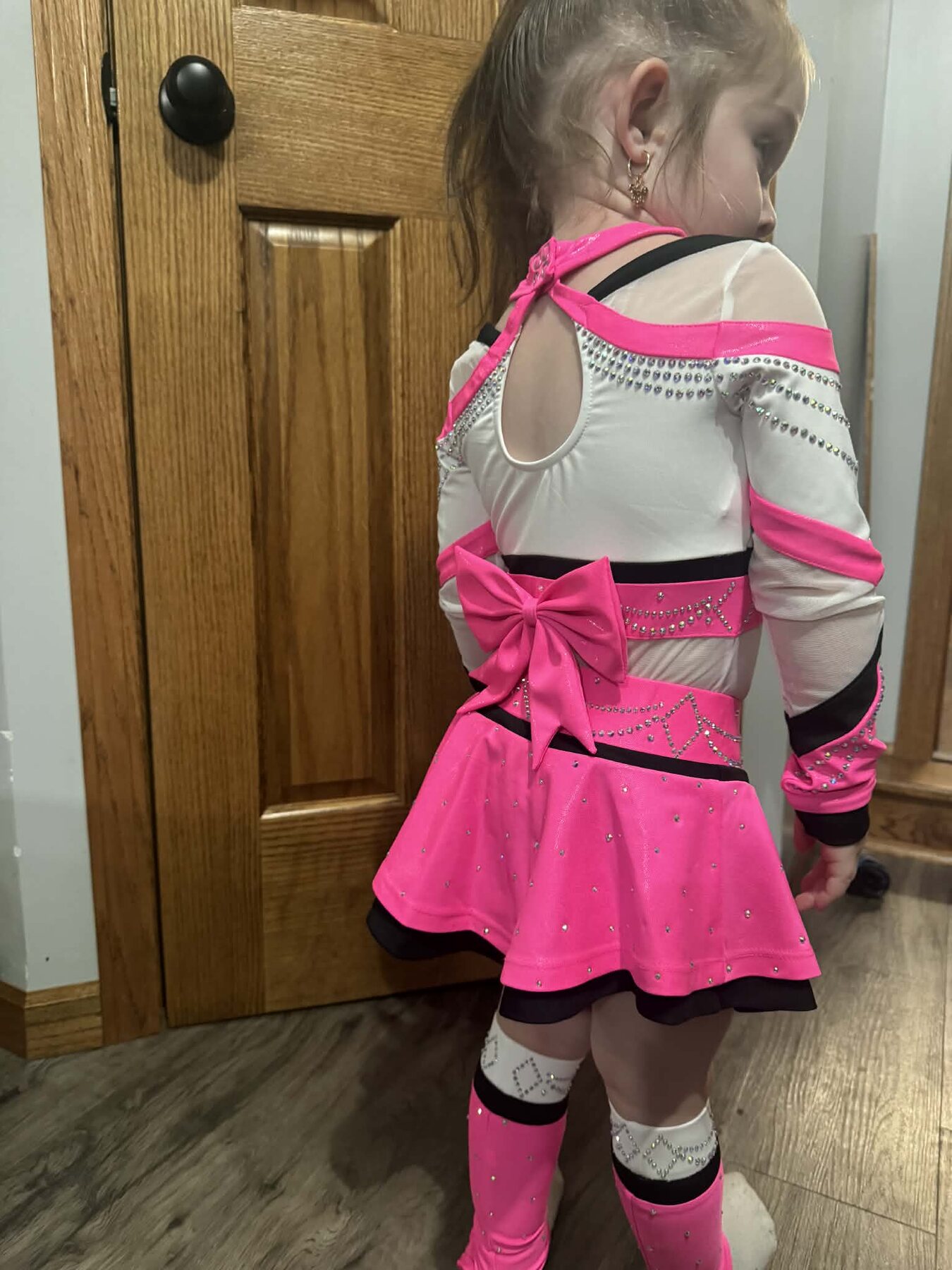 Back view of a hot pink, white, and black rhinestone cheer uniform with a statement bow